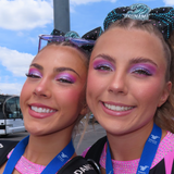 Two cheerleaders women with coluorful makeup and sparkling accessories, smiling outdoors.