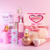 A beauty gift set from Glitter Girl featuring pink and gold cosmetic products including shimmer drops in a bottle, lip gloss, face shimmer puff and a fluffy pink brush, arranged in front of branded packaging boxes on a solid pink background.